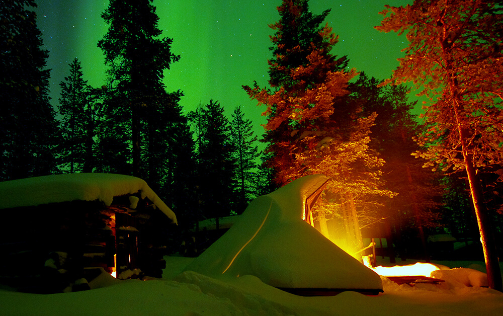 Polarlichter am Himmel über der verschneiten Hütte. 
