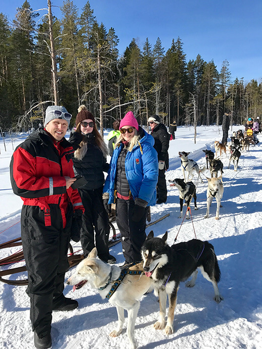 Eine kleine Gruppe Menschen steht neben einem Hundeschlitten mit Huskys.