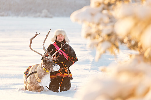 Ein Sami kniet neben seinem Rentier im Schnee.