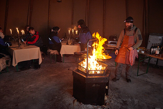 In einem Tipi bereitet ein Mann über dem offenen Feuer ein Essen zu.