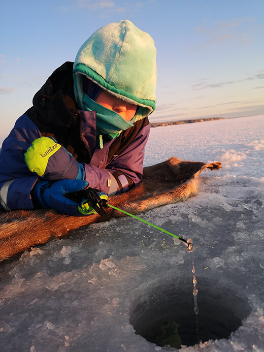 Ein Kind liegt auf dem Eis und versucht einen Fisch zu angeln.