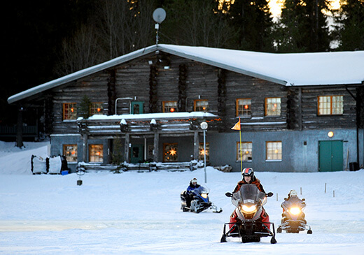 Drei Schneemobile fahren in der Dämmerung von der Lodge weg.