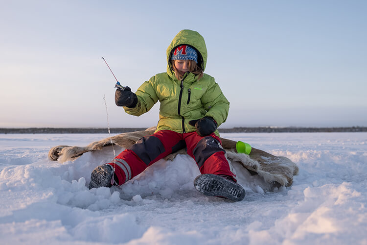 Ein Kind sitzt auf dem Eis und angelt