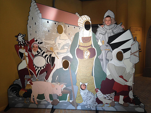 Kinder stecken ihre Köpfe durch eine Wand mit diversen Burgfiguren.