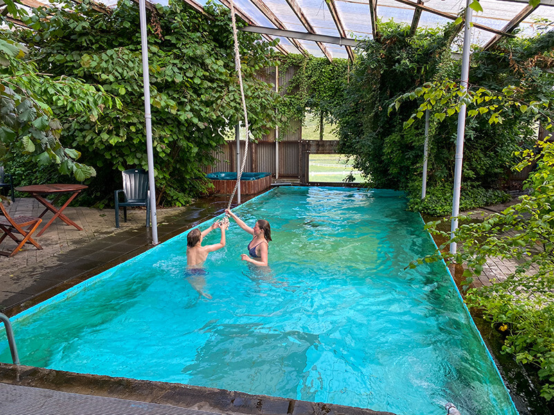 Zwei Kinder baden in einem Pool in einem Gewächshaus.