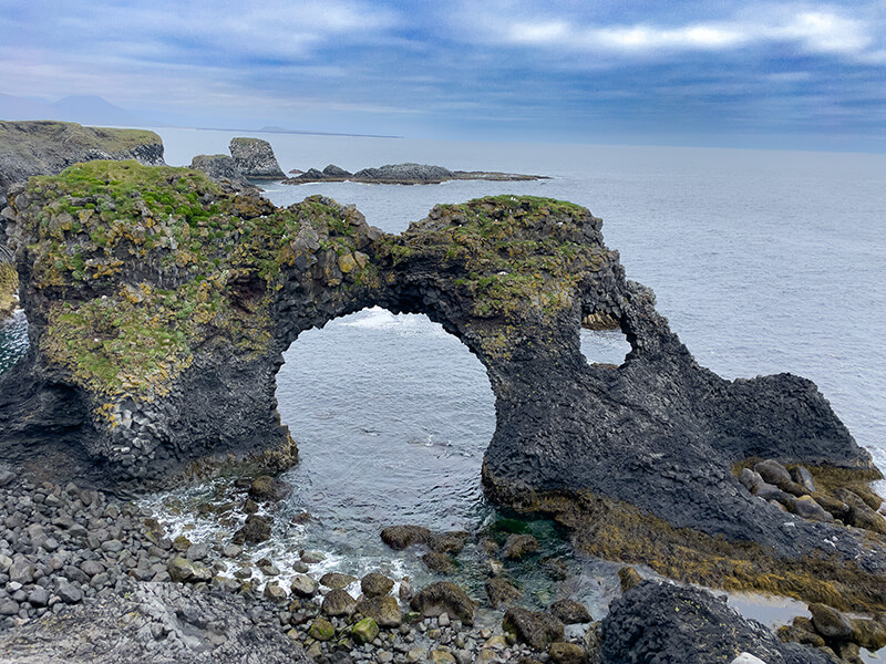 Natürliche Felsformation mit zwei großen Bögen an einer felsigen Küste und ruhigem Meer im Hintergrund.