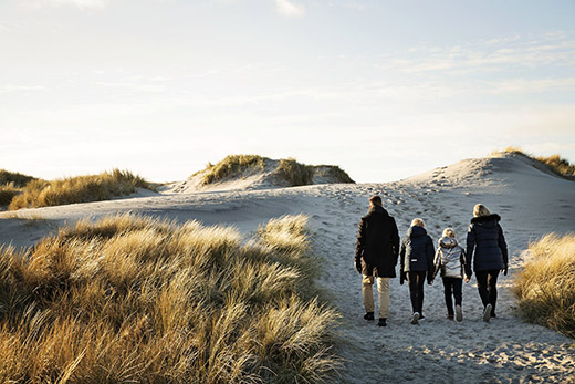 Eine vierköpfige Familie läuft in der Abendsonne über die Dünen.