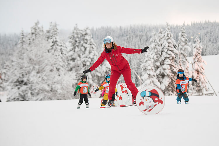 Kinder lernen mit einer Skilehrerin das Skifahren