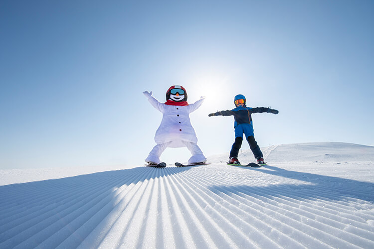 Das Maskottchen Valle mit einem Kind auf dem Skihang