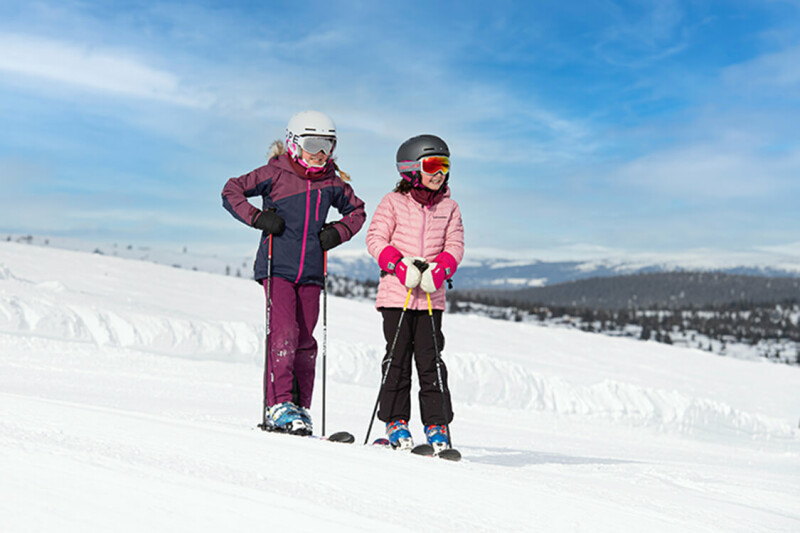 Zwei Mädchen mit Skiausrüstung stehen auf der Piste.