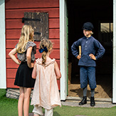 Drei Kinder stehen sich gegenüber vor einem roten Haus