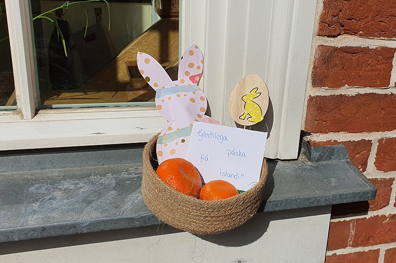 Ein geflochtener Korb gefüllt mit Mandarinen, einem Papier-Osterhasen und einem Ostergruß steht auf der Fensterbank.