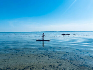 Ein Mädchen paddelt mit einem SUP-Board auf dem klaren Wasser.