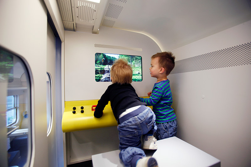 Zwei kleine Kinder im Zug vor einem Bildschirm