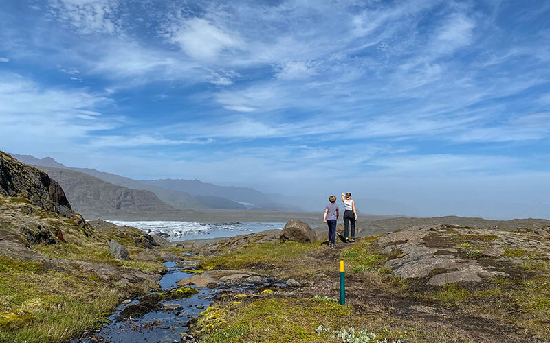 Zwei Kinder laufen auf einem Wanderweg und in der Ferne sieht man Gletscherzungen