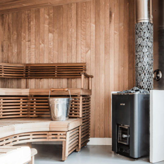 Blick in eine Sauna mit Ofen und Wassereimer.