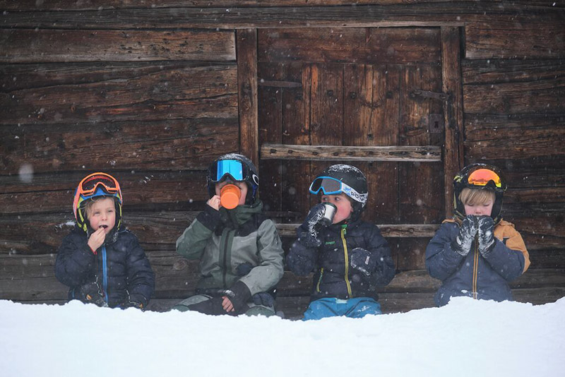 Vier kleine Jungs machen vor einer Hütte eine Pause und trinken aus Bechern.