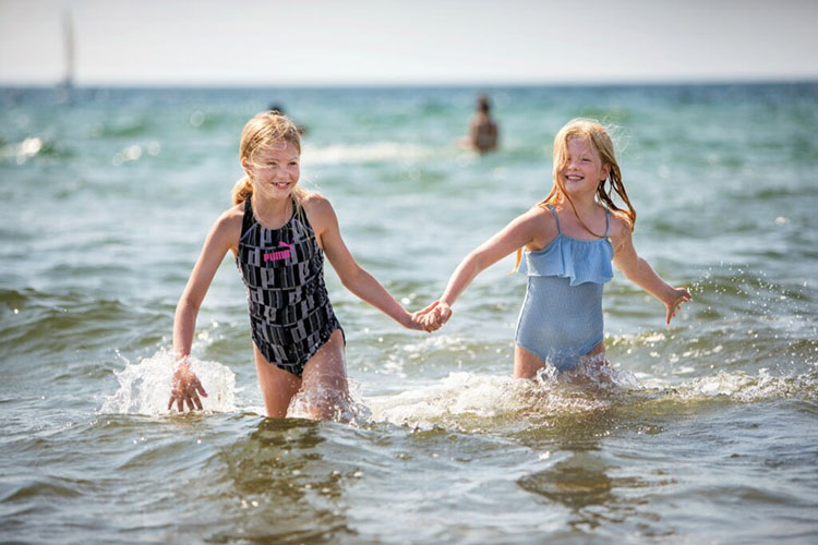 Zwei Mädchen laufen im Meer und halten sich an den Händen. 