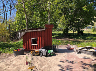 Kleines rotes Spielhaus mit Sandkasten und Spielzeug.