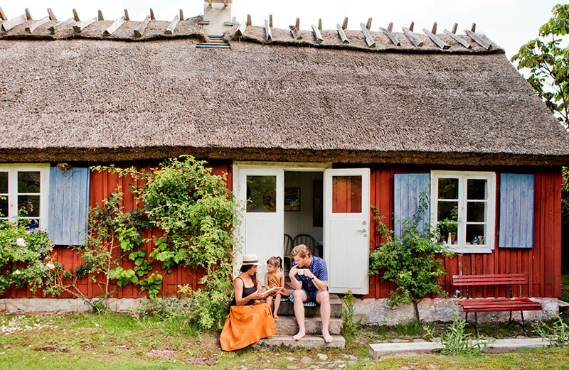 Eine dreiköpfige Familie sitzt auf den Stufen vor einem alten roten Häuschen.