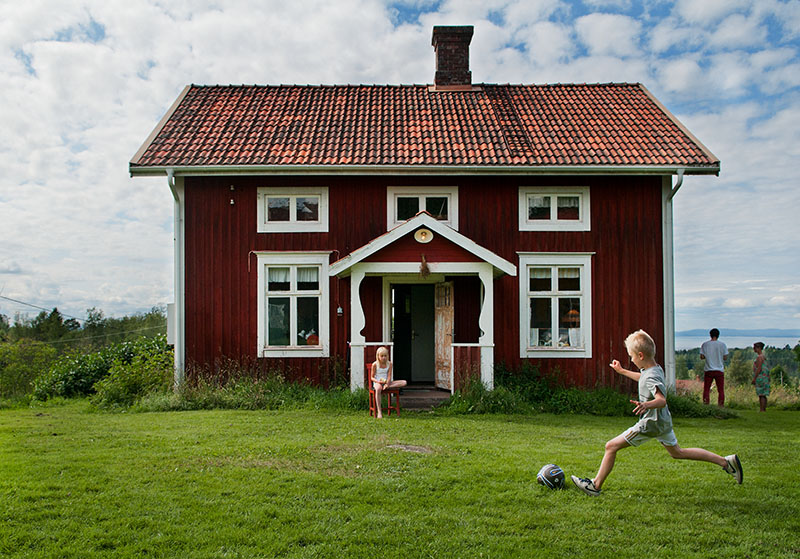 Ein kleiner Junge spielt vor einem roten Haus Fußball.