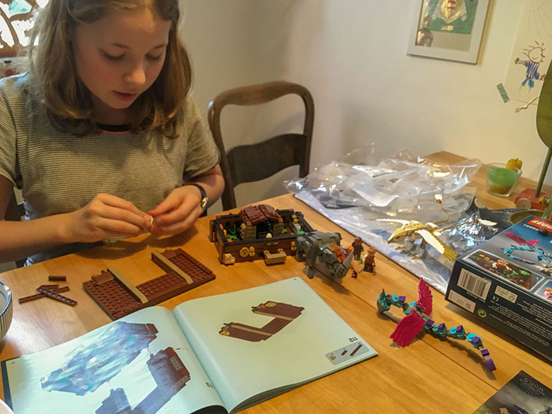Ein Mädchen sitzt am Tisch und baut ein Lego Set nach Anleitung.