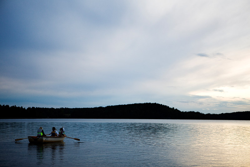 Ein kleines Ruderboot mit drei menschen an Bord gleitet über einen See in der Dämmerung.