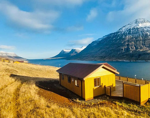 Ein gelbes Haus vor einer Fjordlandschaft.