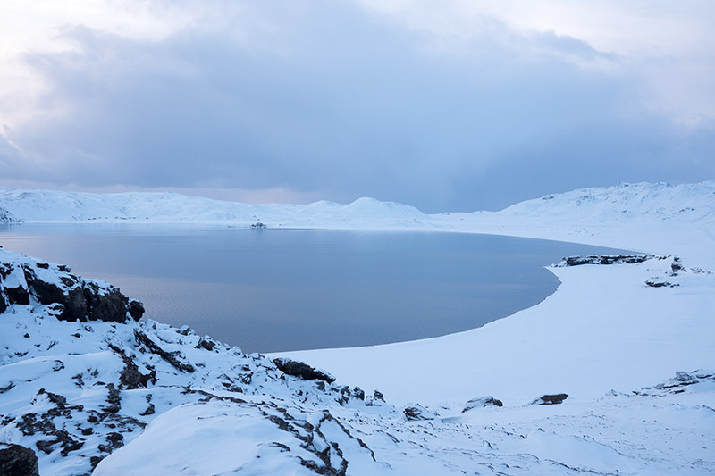 Eine Lagune und umliegende schneebedeckte Hügel.