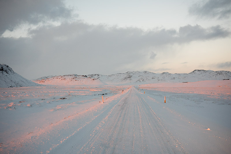 Eine verschneite Landstraße im dämmrigen Licht.