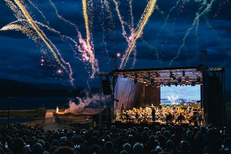 Konzert bei Nacht. Blick auf Bühne mit Feuerwerk im Hintergrund.