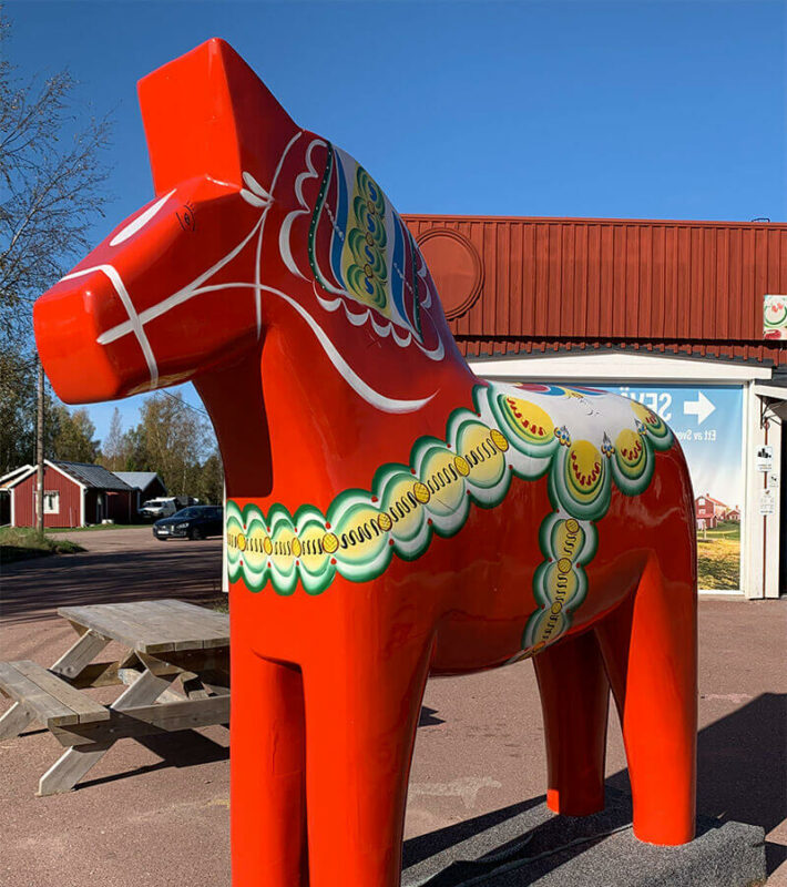 Ein großes rotes Dalapferd vor einer Picknickbank.