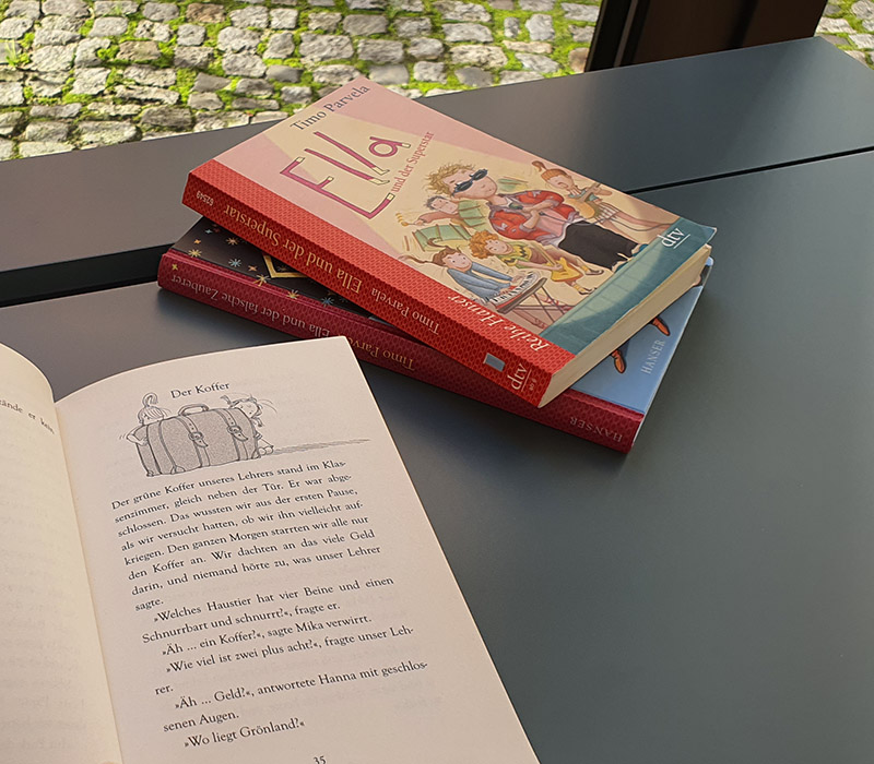 Ein Taschenbuch ist aufgeschlagen und im Hintergrund liegen zwei weitere Bücher.
