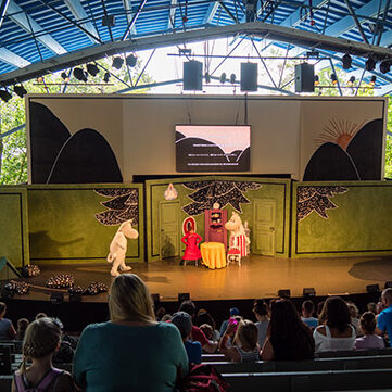 Blick auf eine Theaterbühne von den höheren Rängen. Auf der Bühne stehen kostümierte Muminfiguren.