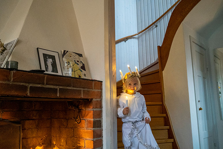 Ein kleines blondes Kind mit Lichterkranz im Haar kommt die Treppe herunter.