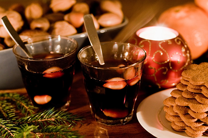 Zwei Tassen von Glögg mit Mandeln stehen neben einem Teller mit Weihnachtsgebäck.