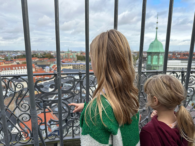 Zwei blonde Mädchen stehen am Metallgitter und schauen über die Dächer der Stadt Kopenhagen.