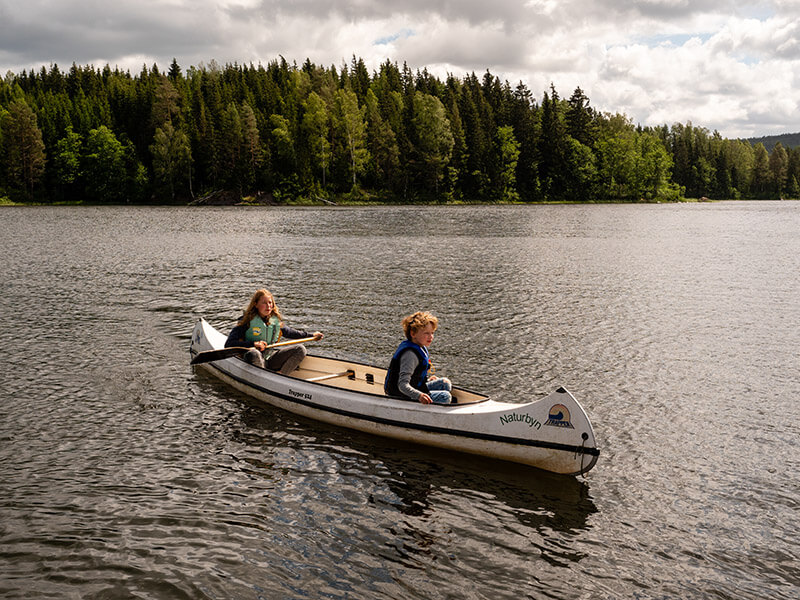 Zwei Kinder sitzen in einem großen weißen Kanu und fahren über den See