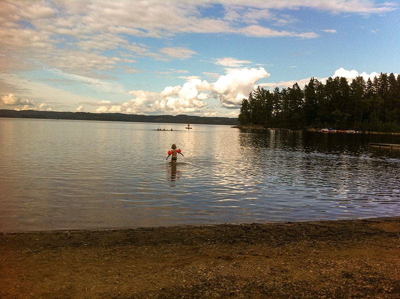 Kleinkind mit Schwimmärmeln steht im Wasser in Ufernähe eines Sees