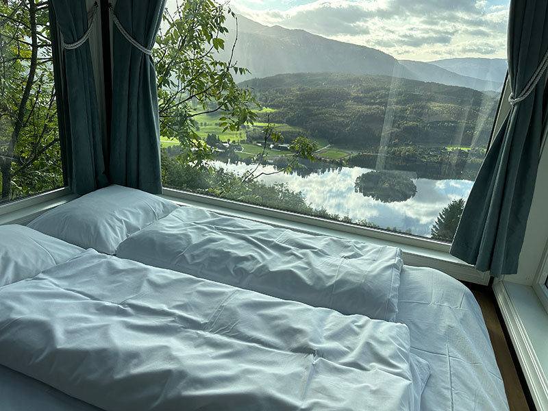 Ein Bett am Fenster mit Blick auf den darunterliegenden Fjord.