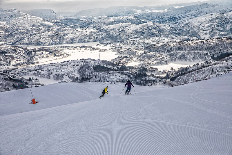 Ein Skifahrer und ein Snowboardfahrer fahren auf einem steilen Abhang Richtung Tal.