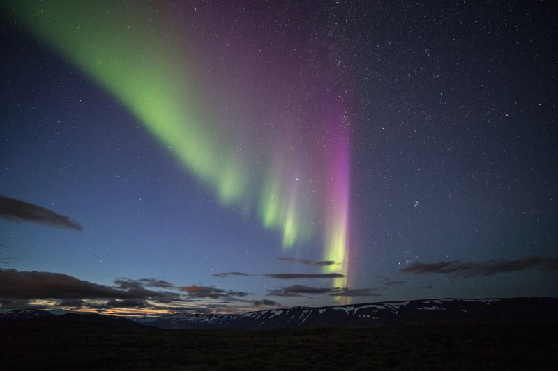 Grüne und violette Nordlichter über einer Bergkette in Island. 