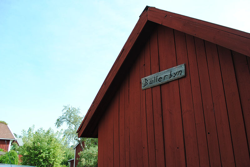 Fassade eines roten Holzhauses mit einem Holzschild mit der Aufschrift "Bullerbyn".