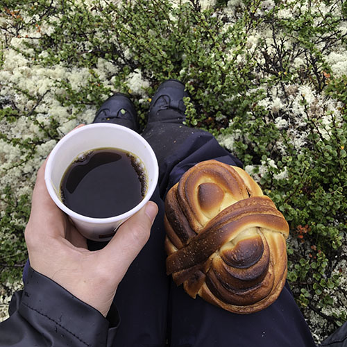 Ein Gebäckstück und ein Kaffeebecher auf dem Schoß.