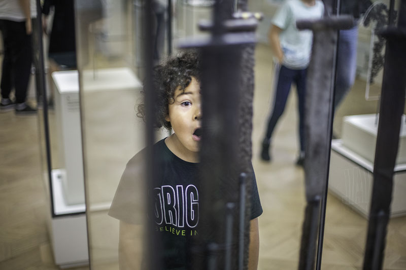Ein kleiner Junge steht vor einer Glasvitrine und hat einen erstaunten Gesichtsausdruck.