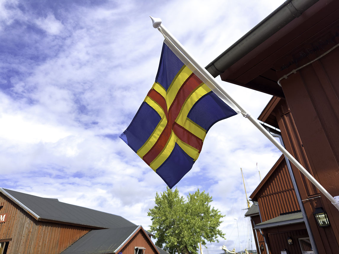 Die Flagge Ålands weht vor einem roten Holzhaus.