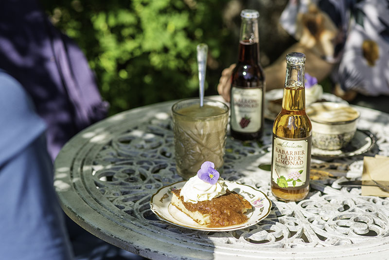 Auf einem kleinen Tisch stehen Limonadenflaschen, Kaffeegläser und ein Teller mit Pfannkuchen.