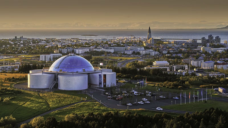 Das Naturkundemuseum Perlan bei Sonnenuntergang. Im Hintergrund ist das Zentrum von Reykjavik zu sehen.