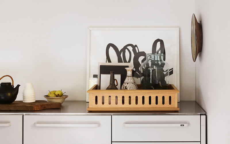 Holztablett mit mehreren Vasen und einem schwarz-weißen abstrakten Bild auf einer weißen Kommode.