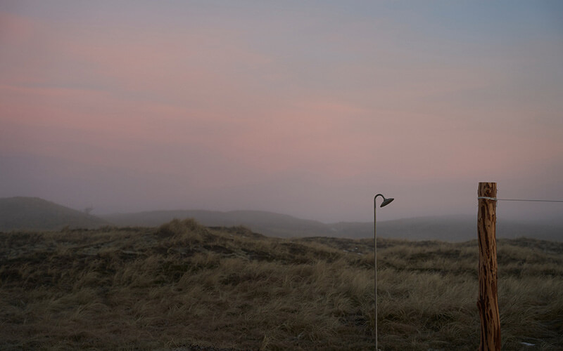Freistehende Außendusche in einer Dünenlandschaft bei Dämmerung.
